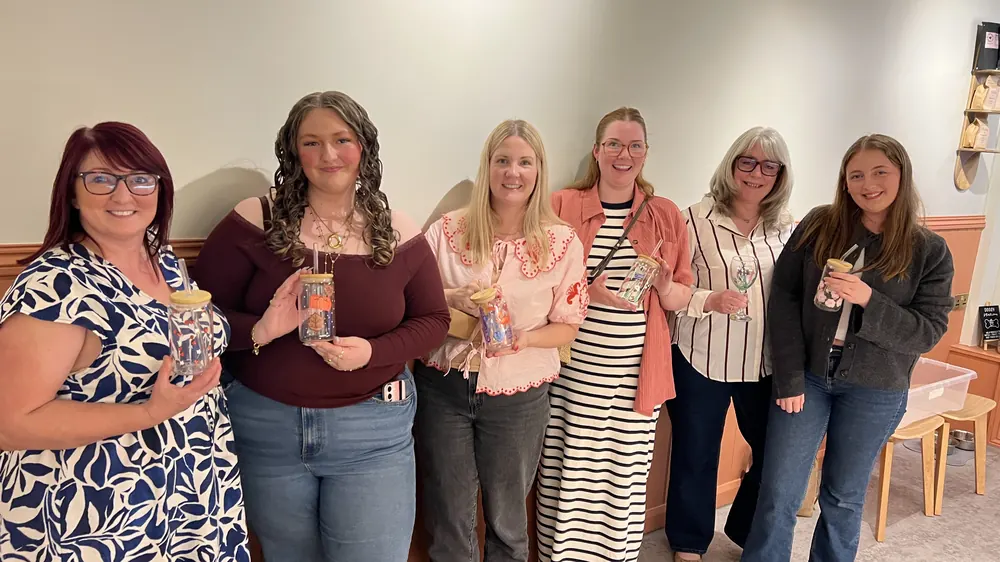 Six guests standing in a row holding the glasses they painted
