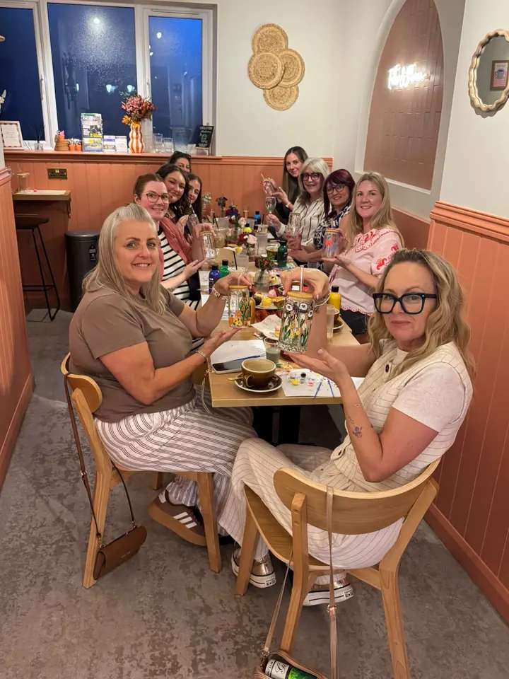 A long table of guests in a café holding up the glass tumblers they have painted