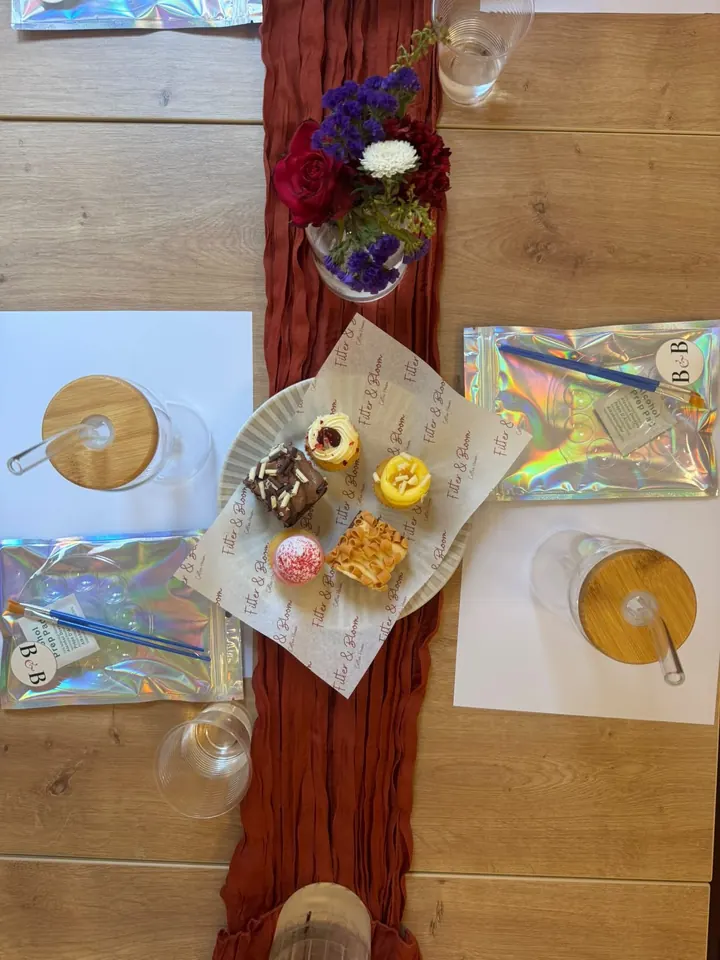 A paint night place setting from above: glass tumblers, brushes, a Blush & Brush kit and a plate of cakes