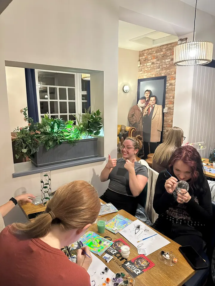 A guest giving two thumbs up while the rest of her table paint their glasses