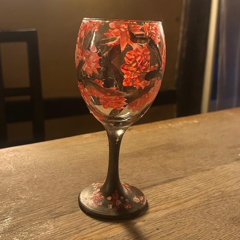 A wine glass painted all over with red flowers, finished at a Blush & Brush paint night